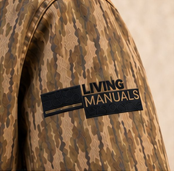 Embroidered Living Manuals logo on a camo jacket sleeve